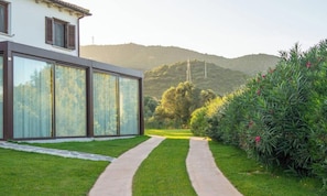 Ein modernes Haus mit großen Glasfenstern, einem gepflasterten Weg und einem üppigen Garten.