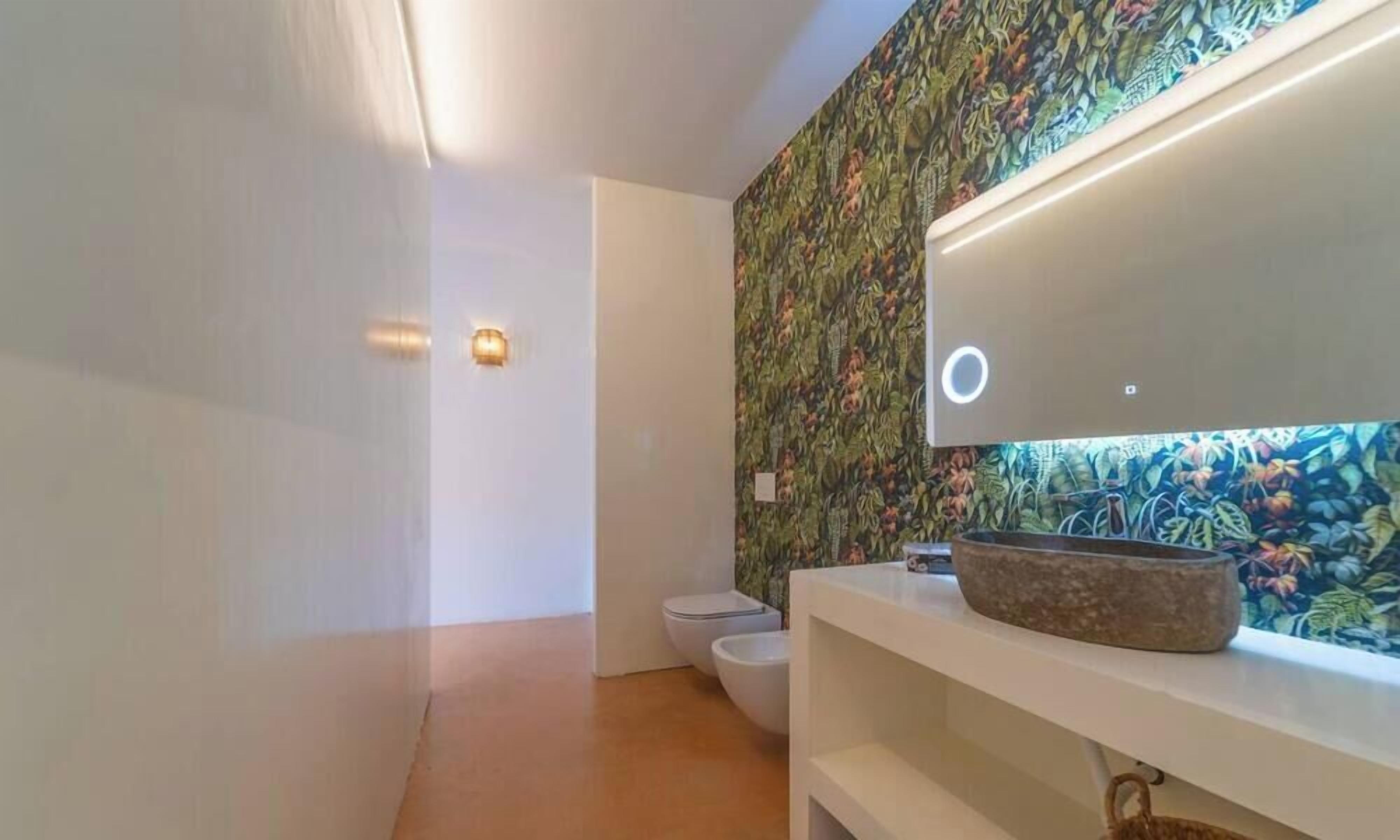 Ein modernes Badezimmer mit Toilette, einem Waschbecken mit Natursteinbecken und einer Wand mit Blumenmuster.