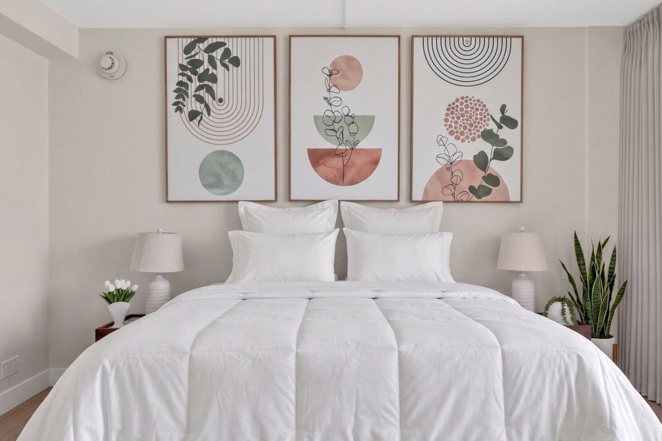Ein Schlafzimmer mit einem Bett, zwei Nachttischen inklusive Lampen und drei an der Wand befestigten Kunstwerken.