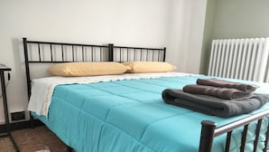 Un lit avec une couvre-lit de couleur turquoise, deux oreillers et des serviettes pliées.