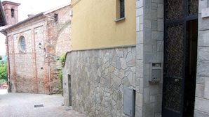 Une rue pavée bordée d’un bâtiment dont la façade est en pierre et qui est agrémenté d’une porte noire richement décorée.