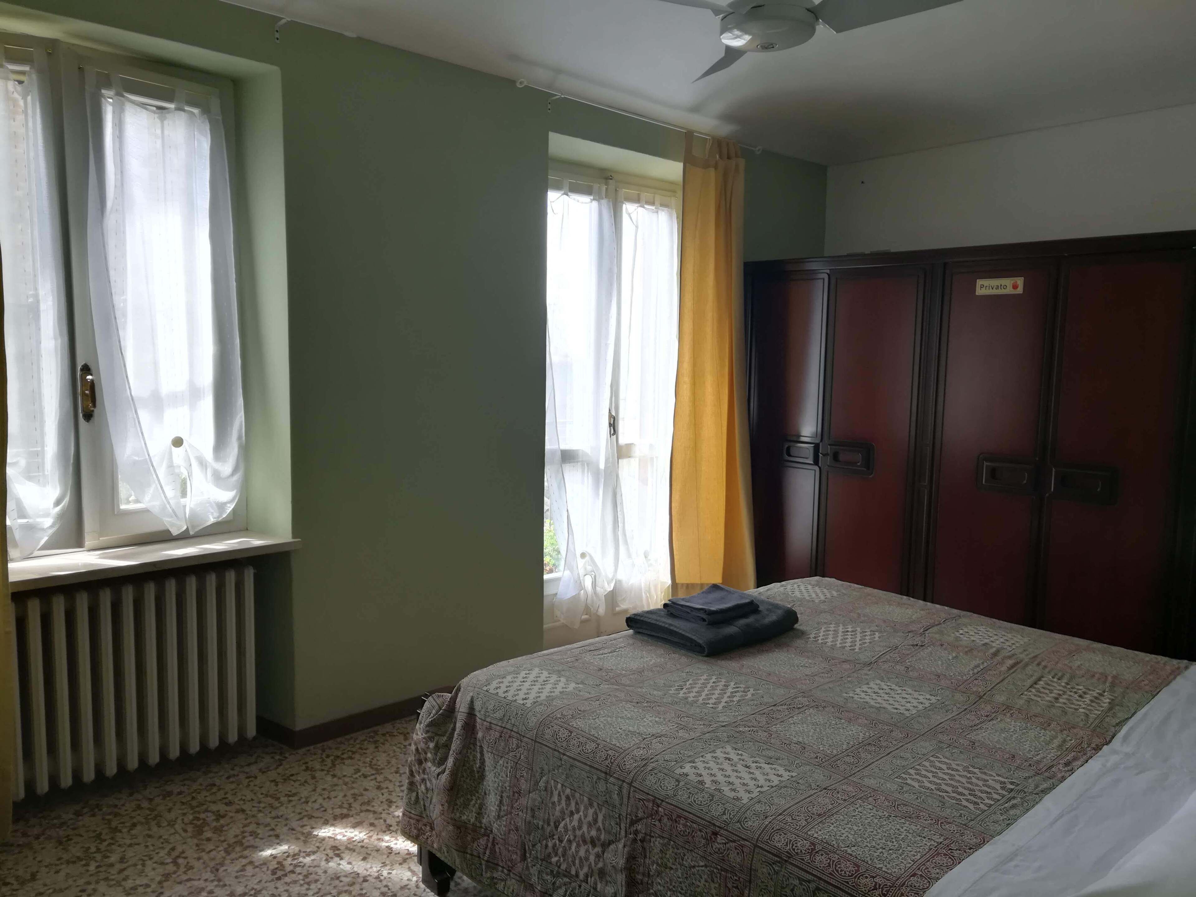 A room with a bed, a radiator, a wardrobe, and a window with curtains.