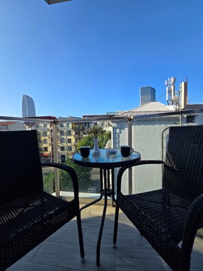 A balcony with two wicker chairs and a small table, overlooking a cityscape with buildings and a clear sky. - Tsereteli Palace (Batumi)