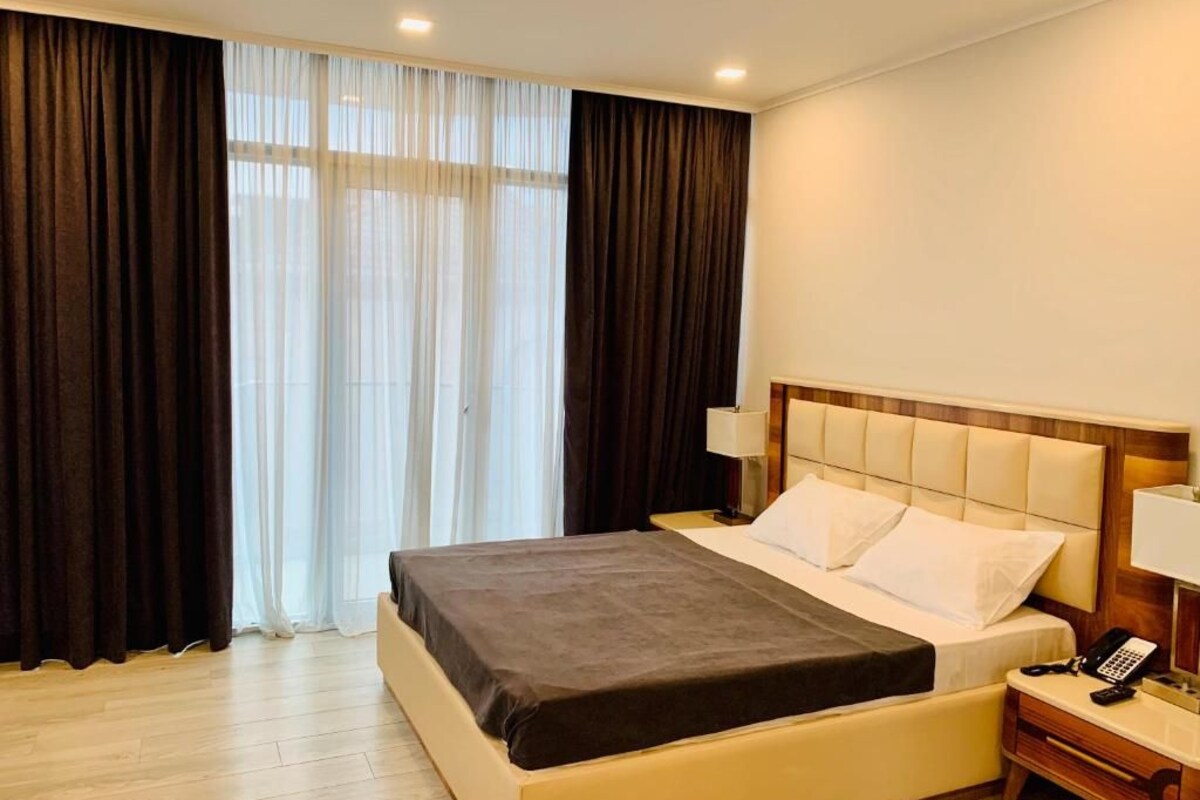 A hotel room with a bed, bedside tables, a lamp, and a phone.