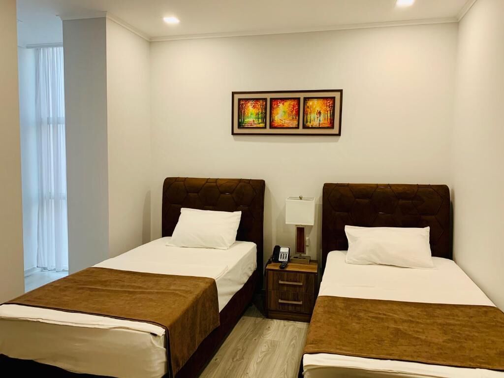 A hotel room with two beds, a nightstand with a lamp, and a painting on the wall.