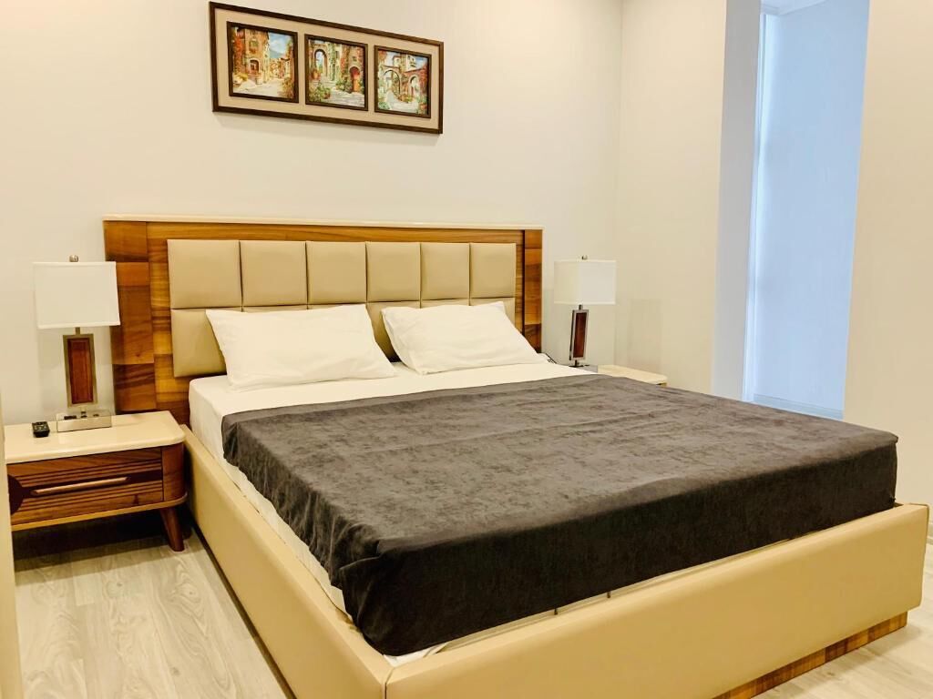 A hotel room with a bed, two bedside tables, a nightstand, a lamp, and a window.