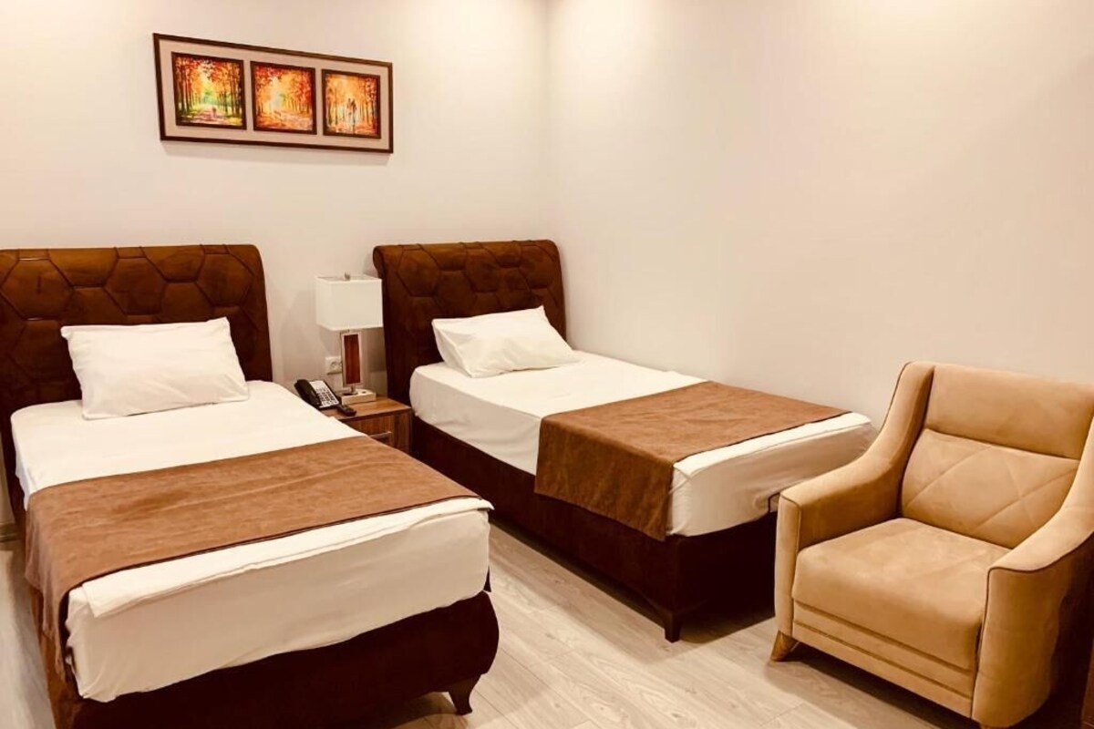 A hotel room with two beds, a chair, and a nightstand with a lamp.
