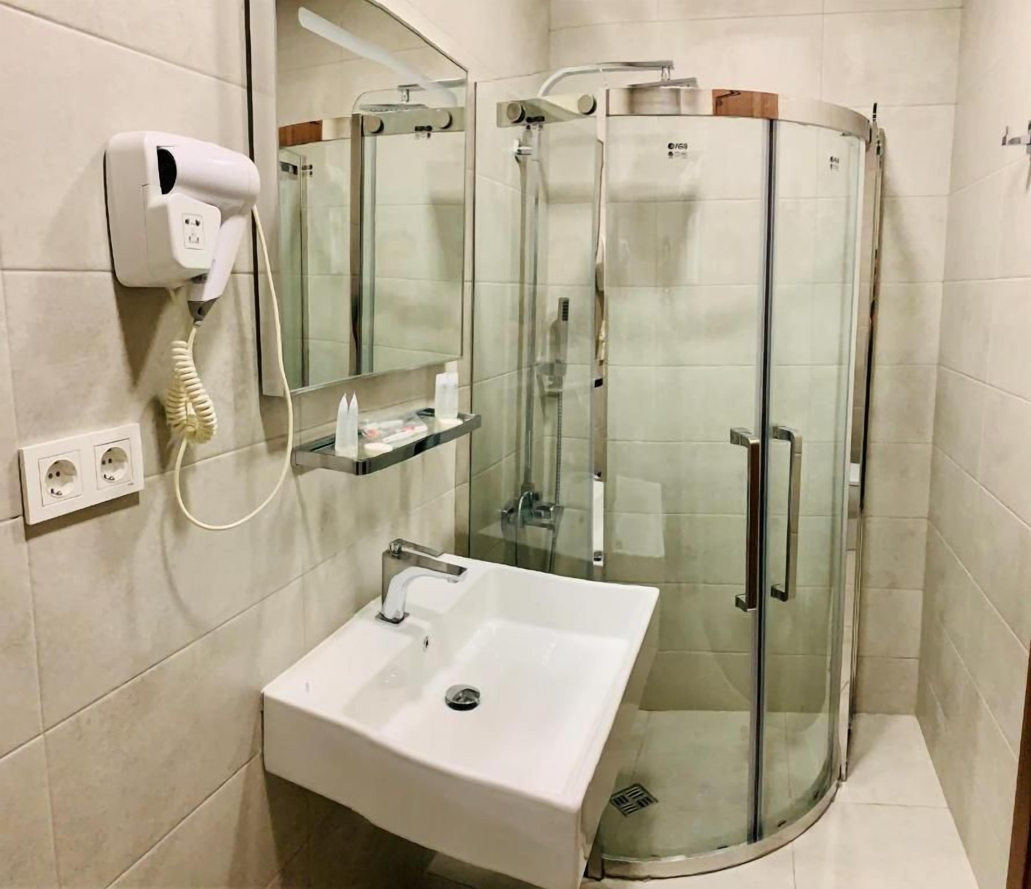 Un baño moderno con ducha envuelta en vidrio, un lavabo blanco y un secador de pelo montado en la pared.