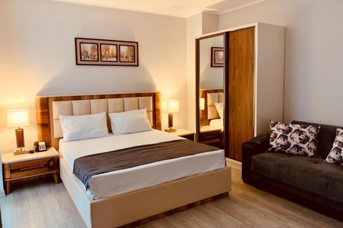 A hotel room with a large bed, bedside lamps, a mirror, a sofa, and framed pictures on the wall.