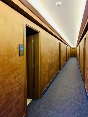 A hotel hallway with wooden walls, carpeted floors, and doors marked with room numbers. - Tsereteli Palace (Batumi)