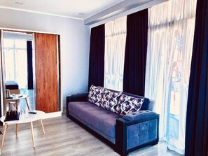Uma sala de estar moderna com sofá, mesa de centro e vista através de amplas janelas com cortinas.