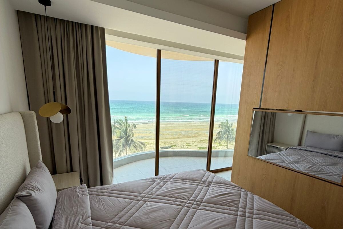 Een hotelkamer met een groot bed, uitzicht op het strand en een houten garderobe.