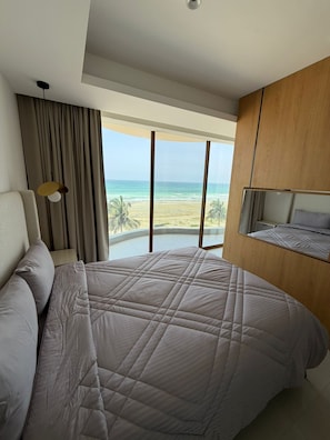 A hotel room with a large bed, a view of the beach, and a wooden wardrobe. - Lamar Residences  (Taqah)