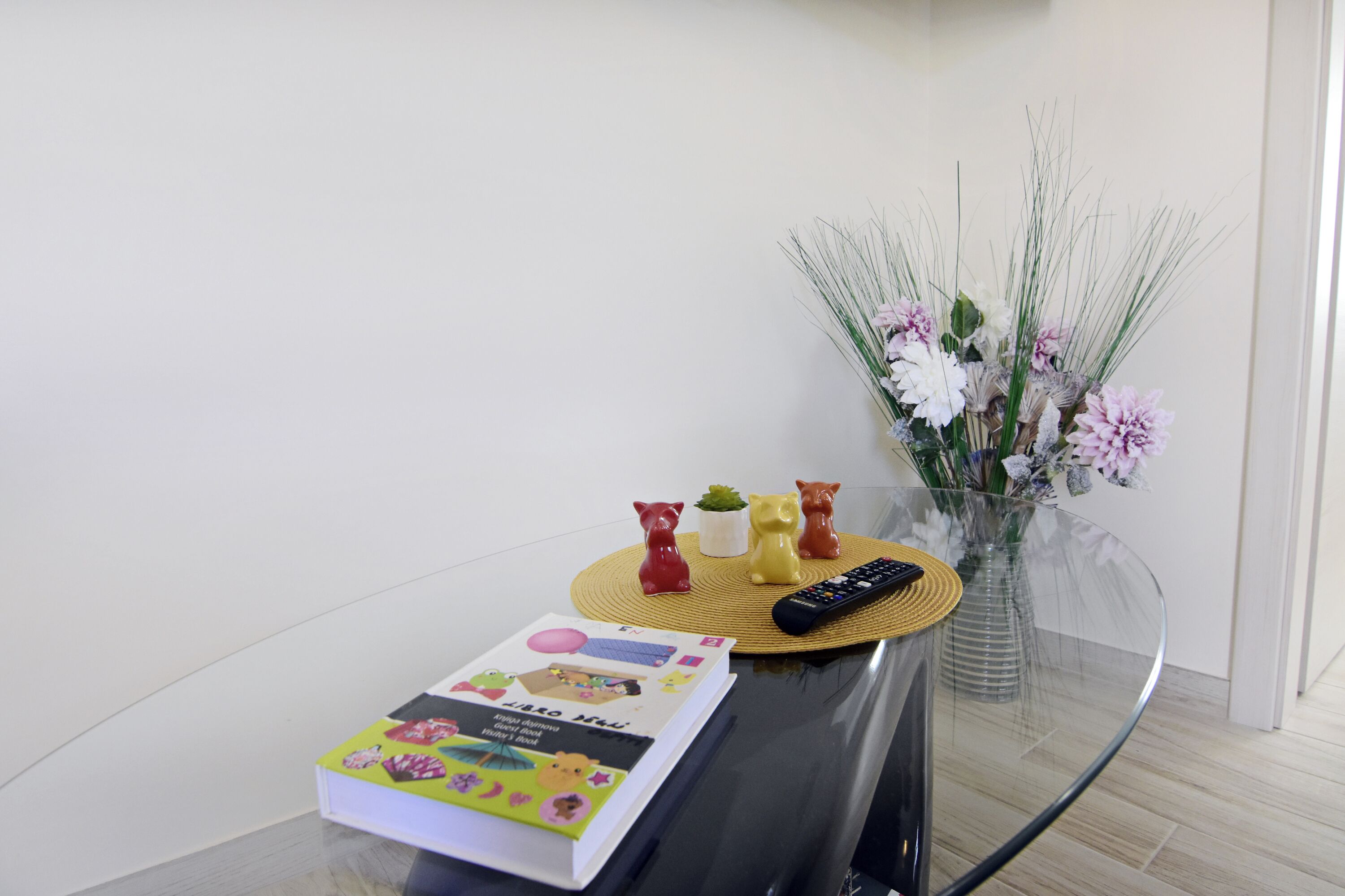 Een glazen tafel met een boek, afstandsbediening en decoratieve voorwerpen.