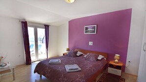 Un dormitorio con una cama grande, una mesita de noche con lámpara, una mesa de vidrio con un florero y vistas al exterior a través de una puerta corrediza.