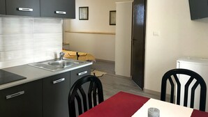 Uma cozinha moderna com armários cinza, uma pia de aço inoxidável e uma área de refeições com mesa vermelha e cadeiras pretas.