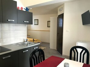 Eine moderne Küche mit grauen Schränken, einer Edelstahlspüle und einem Essbereich mit einem roten Tisch und schwarzen Stühlen.