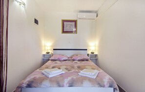 Ett hotellrum med en säng, två sänglampor, en inramad tavla på väggen och en luftkonditioneringsanläggning.
