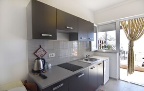 A modern kitchen with dark cabinets, a kettle, a remote, and a window with curtains. - Compact studio stay with sea views and BBQ (Zambratija)
