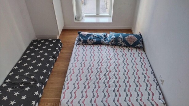Una habitación pequeña con ventana, una cama con ropa de cama estampada y un cojín con diseño de estrellas.