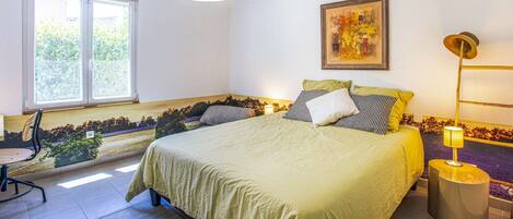 A bedroom with a bed, a window, a painting, an air conditioner, and a lamp.