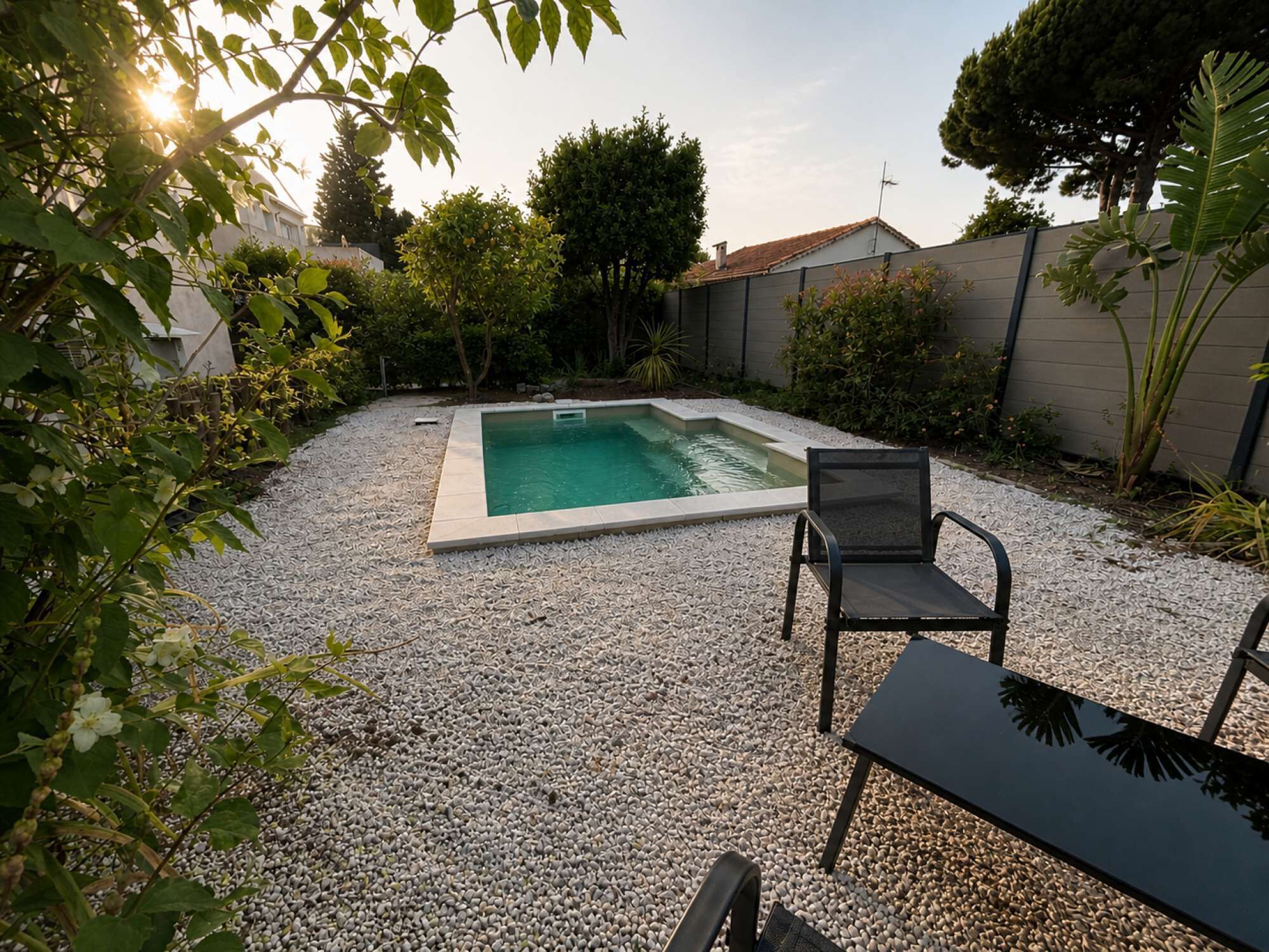 Una piscina rectangular con un área de grava alrededor, una silla negra y una mesa.