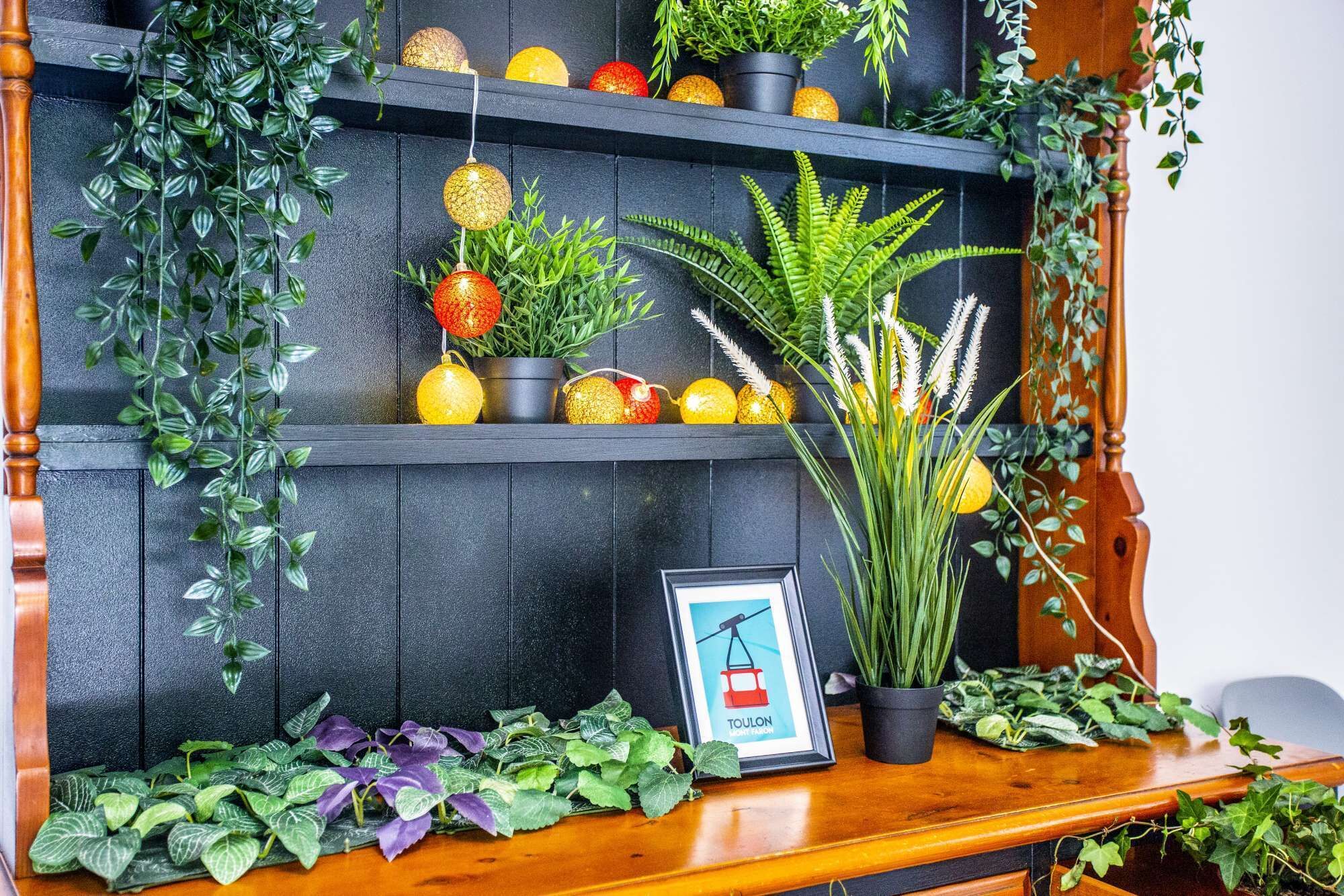 Una estantería de madera con plantas en macetas, esferas decorativas y un cuadro enmarcado.