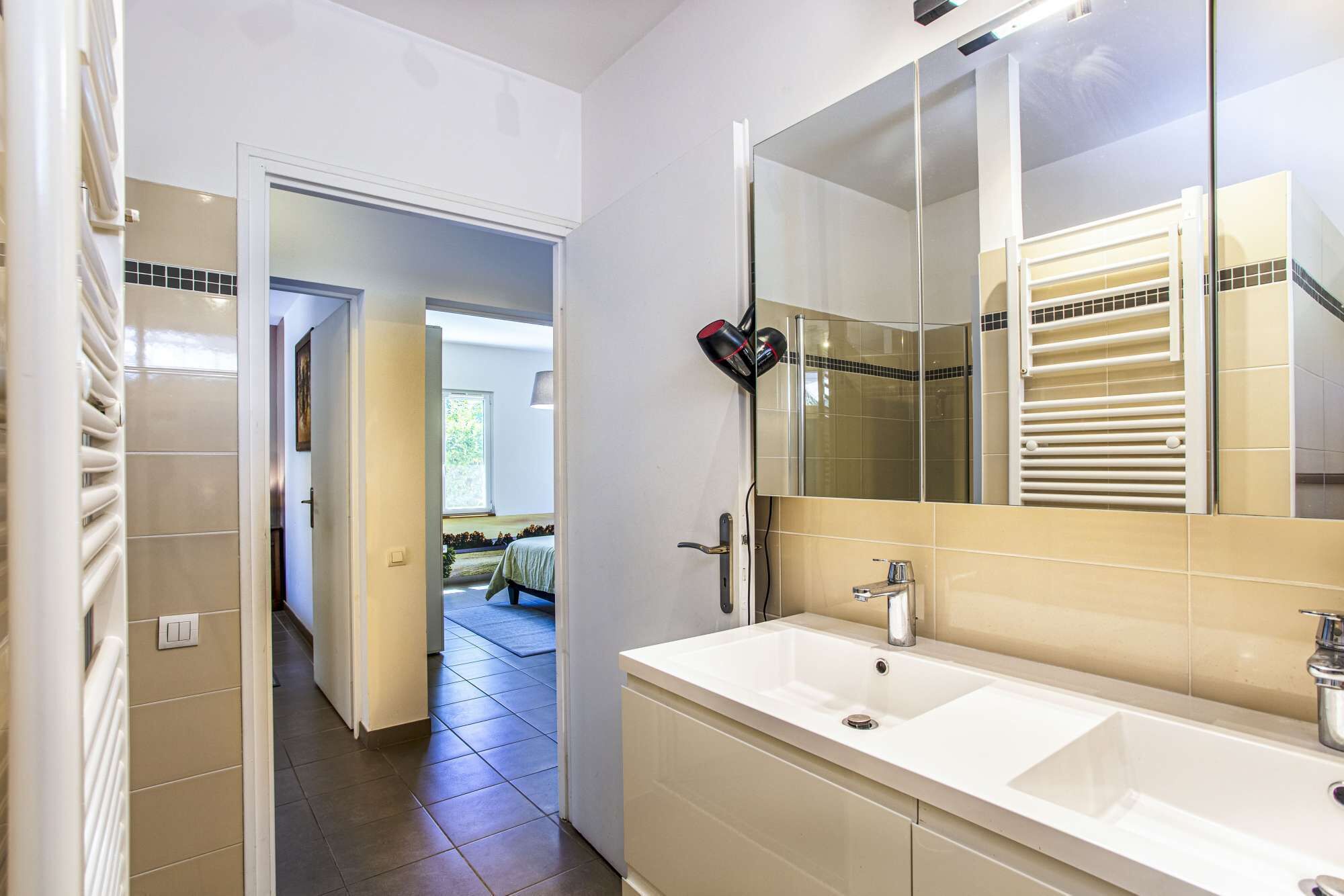 Une salle de bain avec un grand miroir, un lavabo blanc et un porte-serviettes.