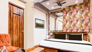 A hotel room with a wooden door, a bed with a headboard, a chair, a coffee table with a kettle, and a patterned wall. - Premium Circus Avenue Rockstar (Kolkata)