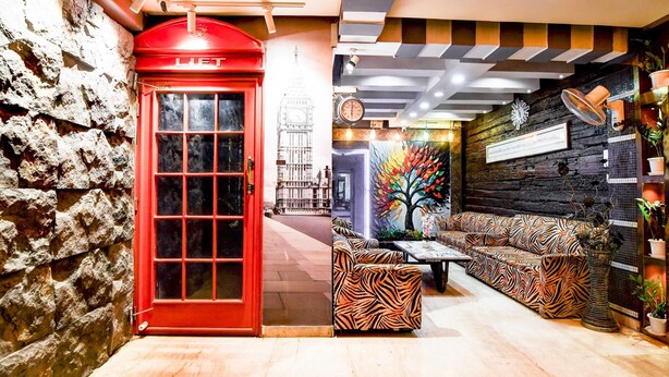 A red telephone booth, a zebra-patterned sofa, and a wall with a clock and a framed picture. - Premium Circus Avenue Rockstar (Kolkata)