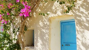 A building with a blue door, a window, and a tree with pink flowers. - Thera Bliss "Olive Tree" Suite Private Pool by ΜΡS (santorini)