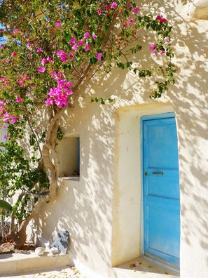 A building with a blue door, a window, and a tree with pink flowers. - Thera Bliss "Olive Tree" Suite Private Pool by ΜΡS (santorini)