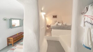 A narrow hallway leading to a bedroom with a bed, a nightstand, and a framed picture on the wall. - Thera Bliss "Olive Tree" Suite Private Pool by ΜΡS (santorini)