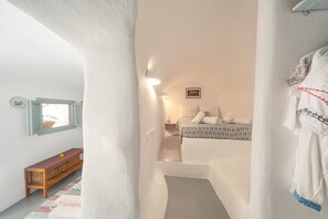 A narrow hallway leading to a bedroom with a bed, a nightstand, and a framed picture on the wall. - Thera Bliss "Olive Tree" Suite Private Pool by ΜΡS (santorini)