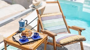 A poolside chair with a striped cushion, a hat, and a tray with a bundt cake, coffee cups, and a blue teapot. - Thera Bliss "Olive Tree" Suite Private Pool by ΜΡS (santorini)