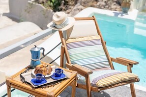 A poolside chair with a striped cushion, a hat, and a tray with a bundt cake, coffee cups, and a blue teapot. - Thera Bliss "Olive Tree" Suite Private Pool by ΜΡS (santorini)
