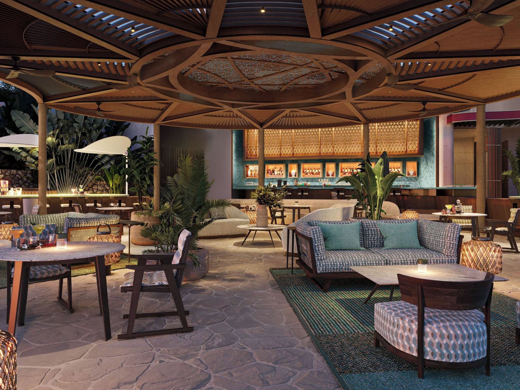 An outdoor seating area with round tables, cushioned seating, and a bar in the background.
