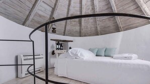 Ein Zimmer mit einem weißen Bett, einem Heizgerät und einer Holzbalkendecke.