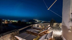 Eine Terrasse mit Liegestühlen und Blick auf eine Küstenstadt bei Nacht.