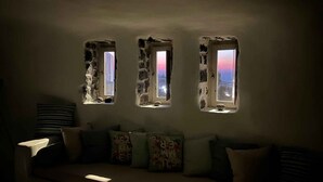 Ein Zimmer mit einer Couch, drei Fenstern mit rustikalen Steinrahmen und Blick auf eine Stadtlandschaft.