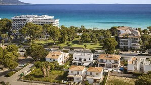 A coastal residential area with a large building, smaller houses, and a clear view of the sea. - Spacious 5-bedroom en-suite villa with pool in stunning Playa de Muro with AC (Muro)