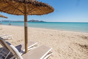 A beach with a thatched umbrella, white lounge chairs, and a clear view of the sea and distant mountains. - Spacious 5-bedroom en-suite villa with pool in stunning Playa de Muro with AC (Muro)