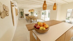 A modern kitchen with a wooden island, a dining area with wicker chairs, and a fireplace. - Spacious 5-bedroom en-suite villa with pool in stunning Playa de Muro with AC (Muro)