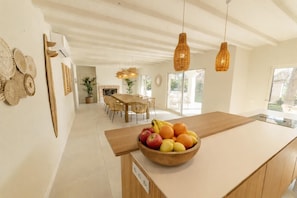 Una cucina moderna con isola in legno, zona pranzo con sedie in vimini e camino.