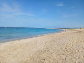 En sandstrand med kristallklart blått vatten och en klar himmel.