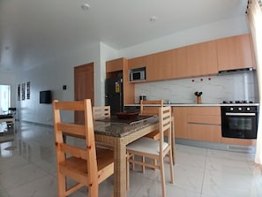 A modern kitchen with wooden cabinets, a dining table with chairs, a microwave, a refrigerator, and an oven.
