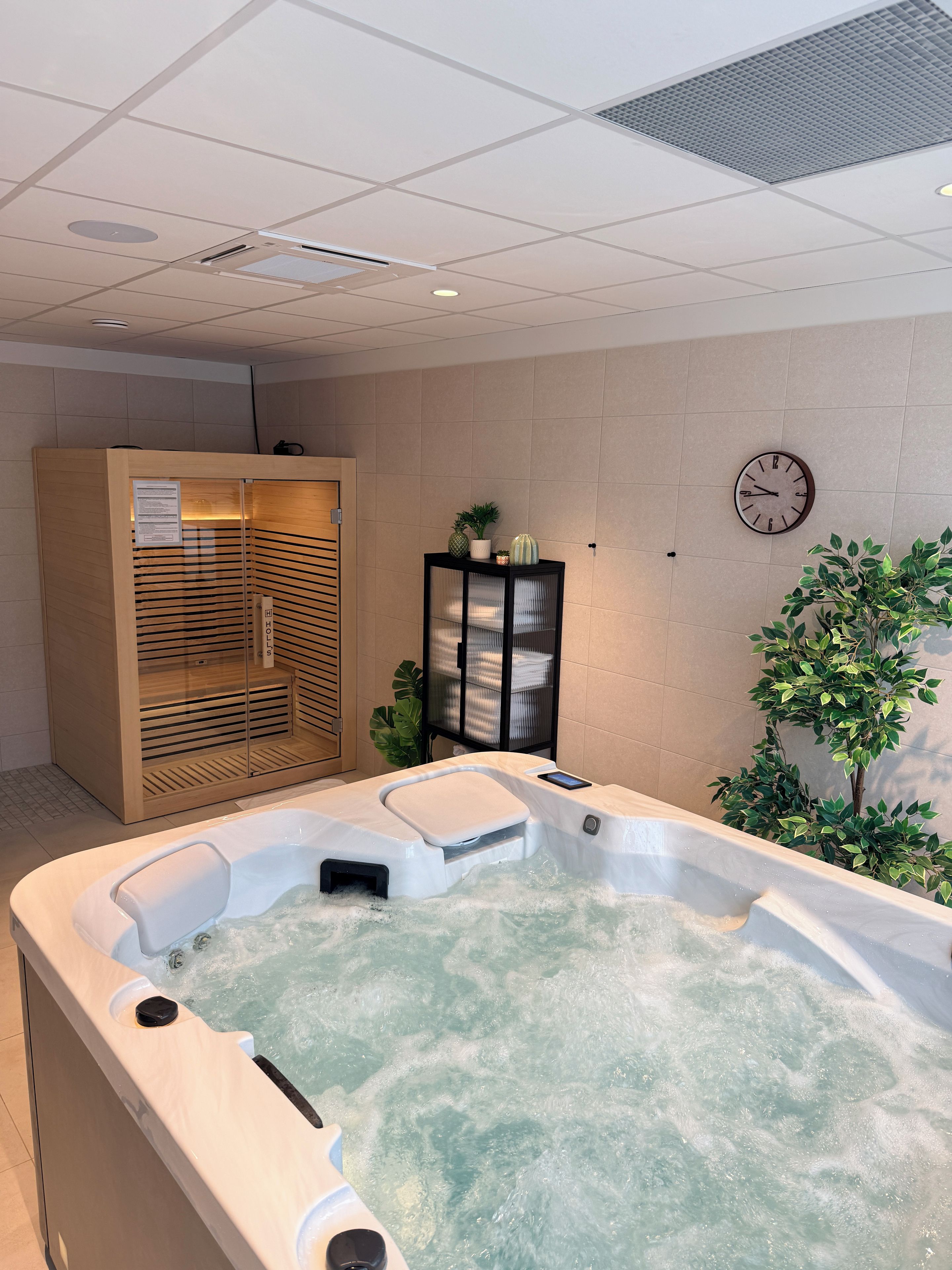Ein Wellnessbereich mit Whirlpool, Holzschrank, einer Uhr und einer Topfpflanze.