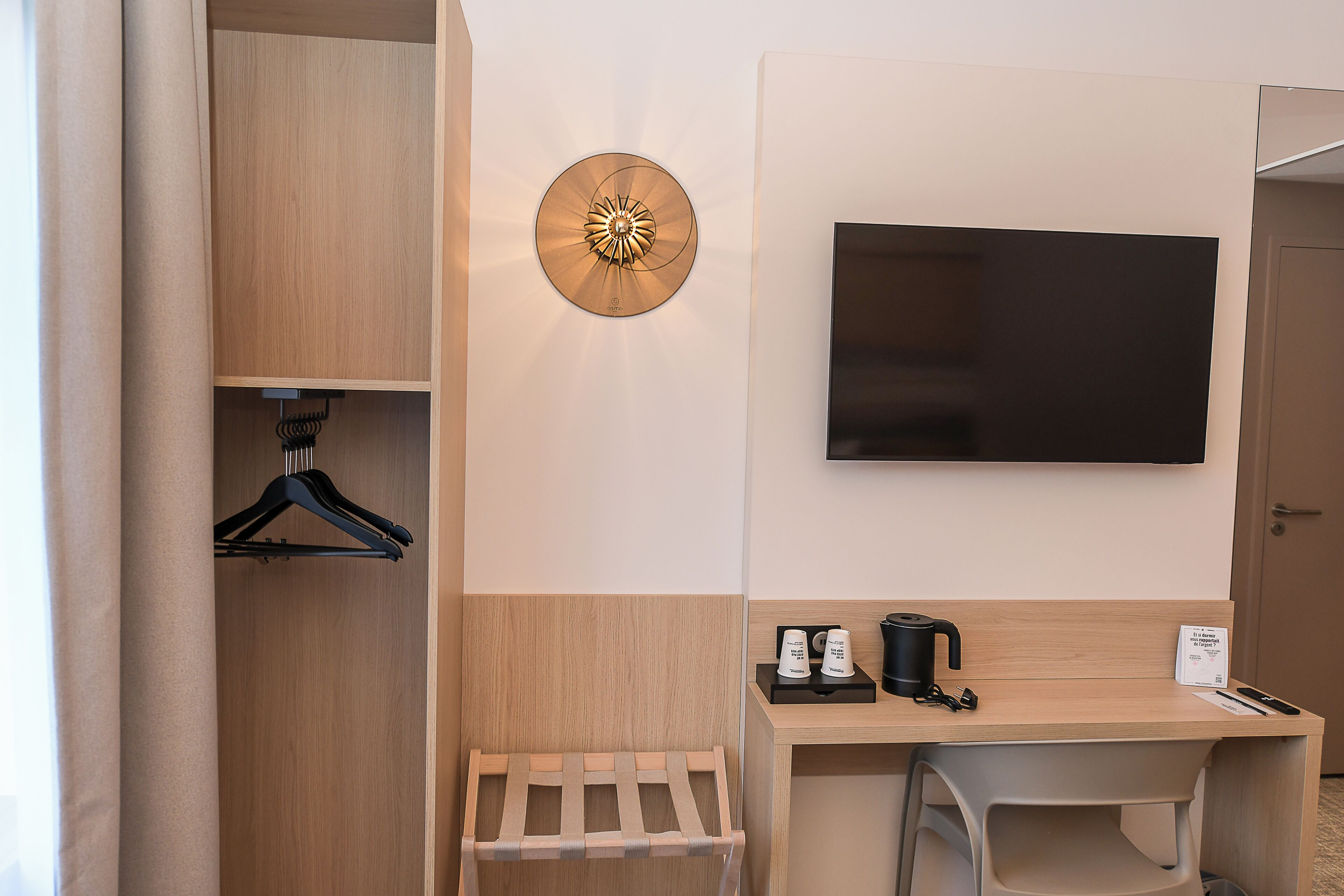 Une chambre d’hôtel équipée d’une armoire en bois, d’un téléviseur fixé au mur, d’un bureau avec une machine à café et d’un porte-manteau mural.