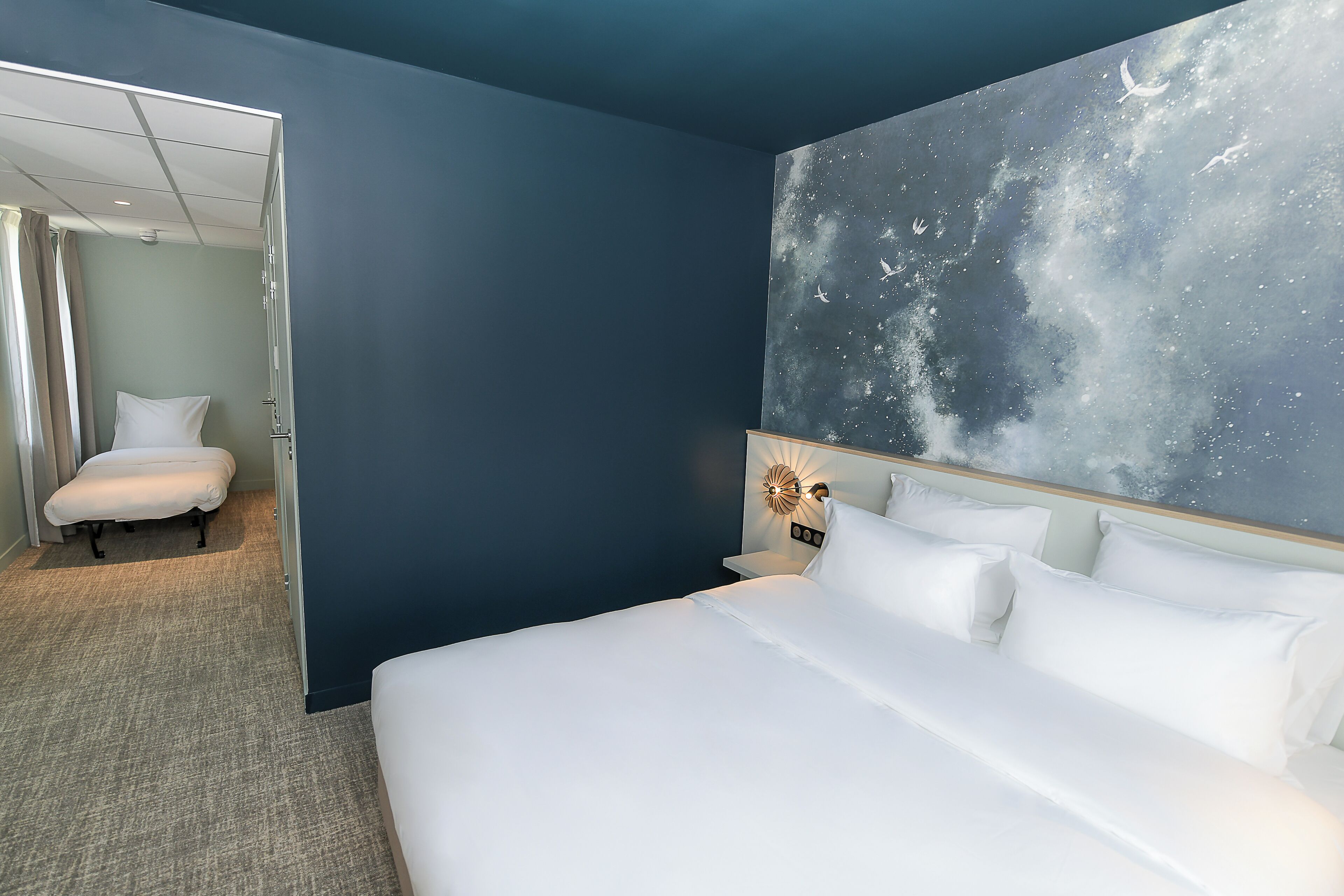 Un dormitorio con cama, mesita de noche, un cuadro de una galaxia y una puerta que da a otra habitación.