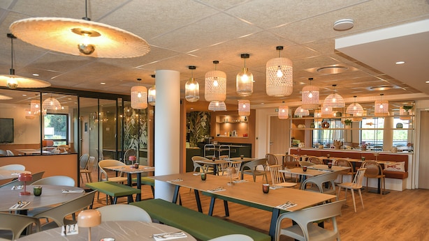 A restaurant with multiple tables and chairs, hanging pendant lights, and a bar area. - The Originals Boutique Osmo Hôtel (Chantepie)